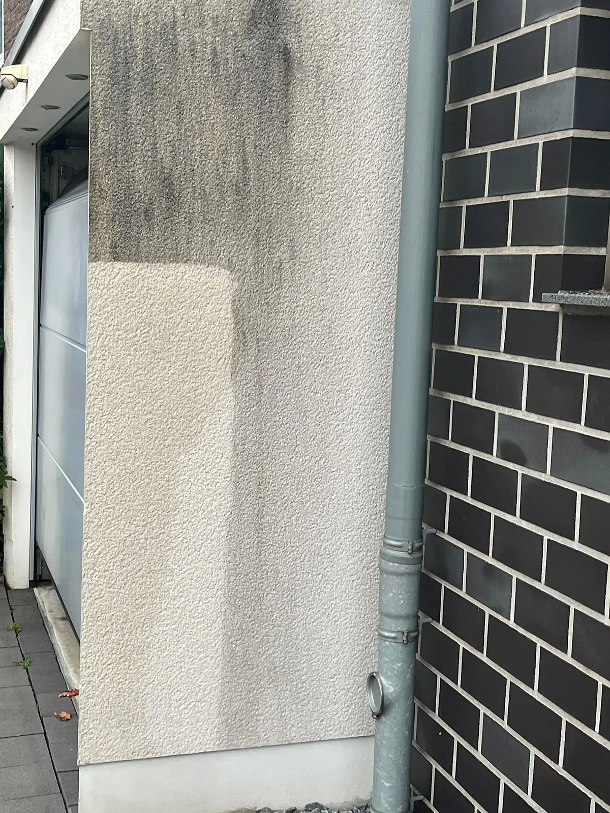 Gereinigter Streifen auf einer verschmutzten Putzfläche neben Klinker